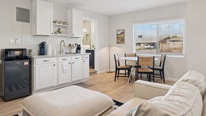 A modern kitchen with white cabinets, a refrigerator, and a dining area with a table and chairs. - Chic & Cozy Studio | King Bed + Sleeper (Tempe)
