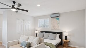 A bedroom with a bed, two bedside tables with lamps, a ceiling fan, a window with blinds, and an air conditioning unit. - Chic & Cozy Studio | King Bed + Sleeper (Tempe)