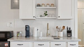 A modern kitchen with white cabinetry, a marble countertop, a coffee maker, and various kitchen utensils. - Chic & Cozy Studio | King Bed + Sleeper (Tempe)