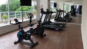 A gym with stationary bikes, treadmills, and a large mirror. - Compacto de luxo - One Milênio Cocô (Fortaleza)