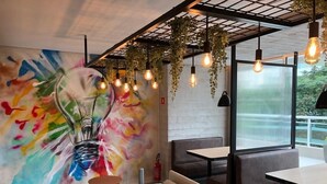 A modern restaurant interior with a vibrant abstract mural, hanging light fixtures, and comfortable seating. - Compacto de luxo - One Milênio Cocô (Fortaleza)