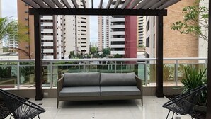 A balcony with a grey sofa, two black chairs, and a pergola. - Compacto de luxo - One Milênio Cocô (Fortaleza)