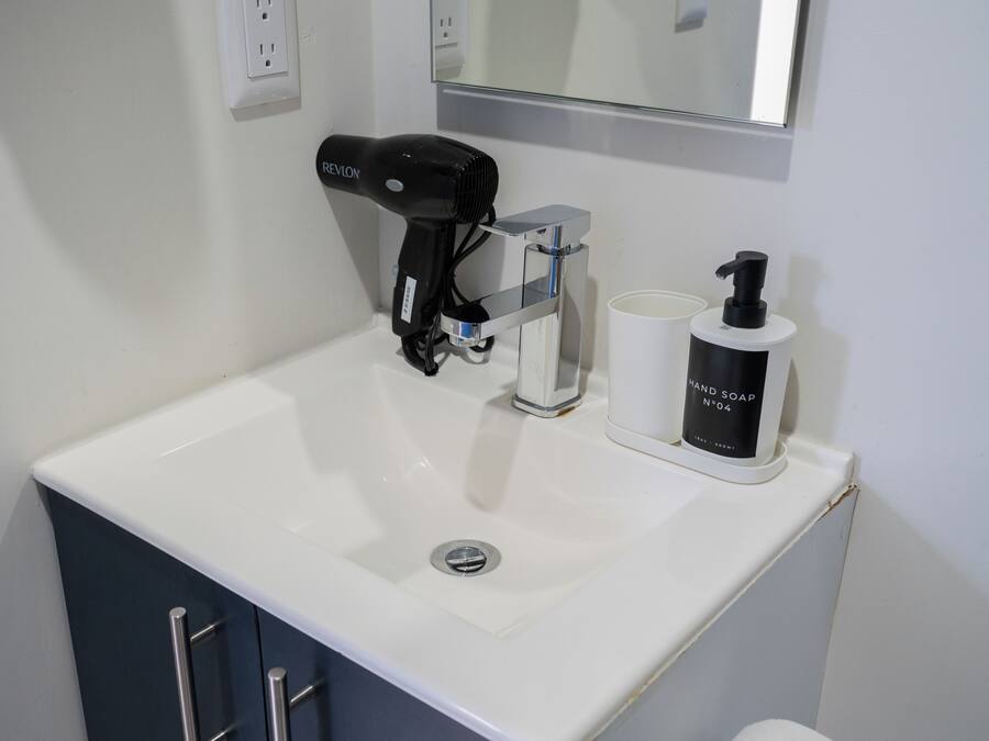 A bathroom sink with a hair dryer, a soap dispenser, and a mirror above.