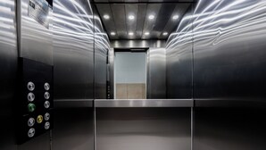 Interior de un ascensor con paredes metálicas, un panel de control con varios botones e iluminación empotrada en el techo.