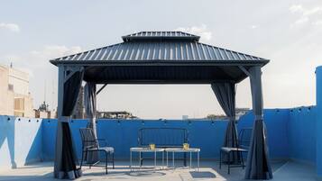 Een terras op het dak met een overdekte zithoek, een tafel en stoelen.