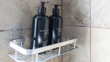 Un baño con un estante metálico que contiene dos botellas negras con las etiquetas 'BODY WASH' y 'SHAMPOO'.