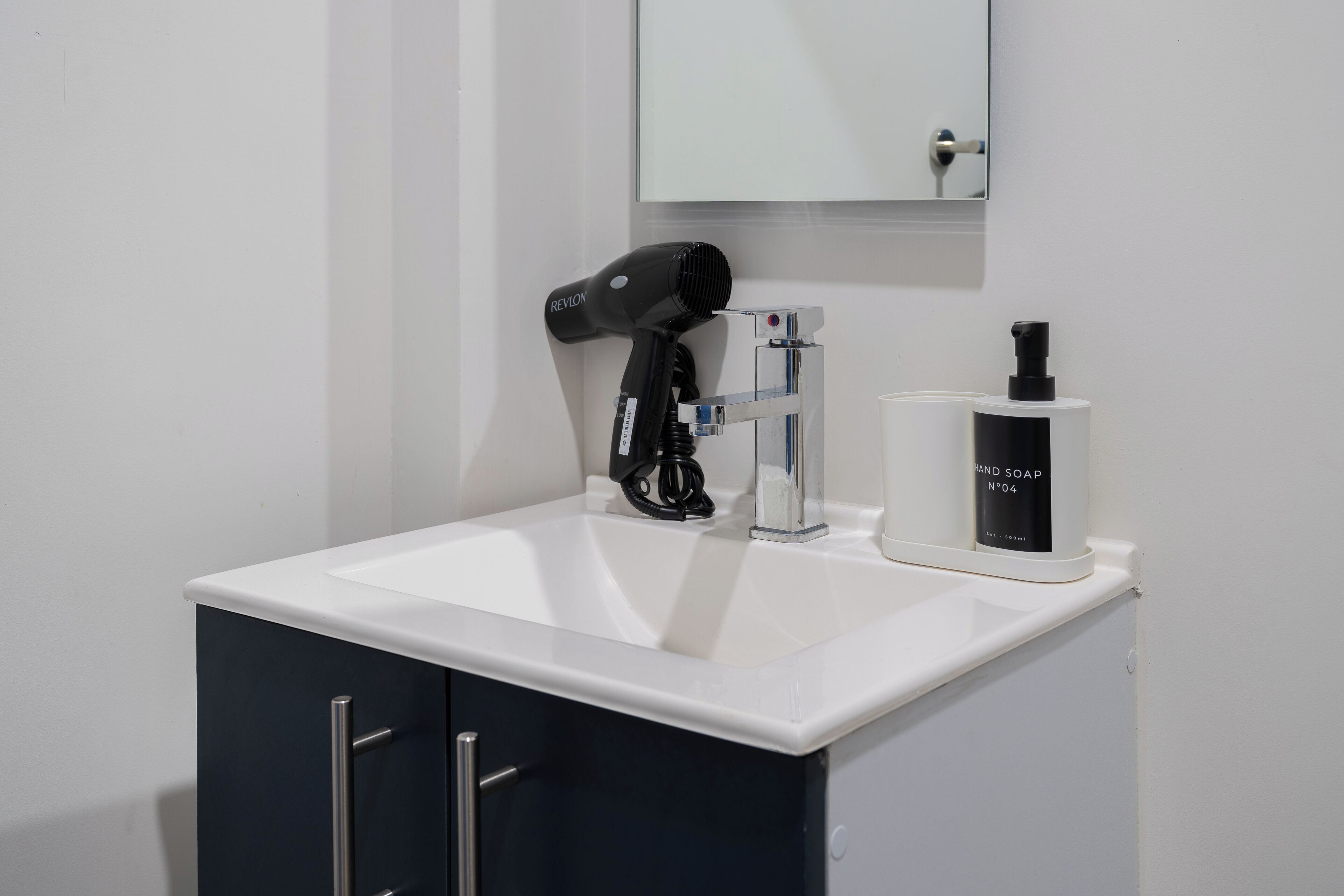 A bathroom with a white sink, a black hair dryer, and a bottle of hand soap.