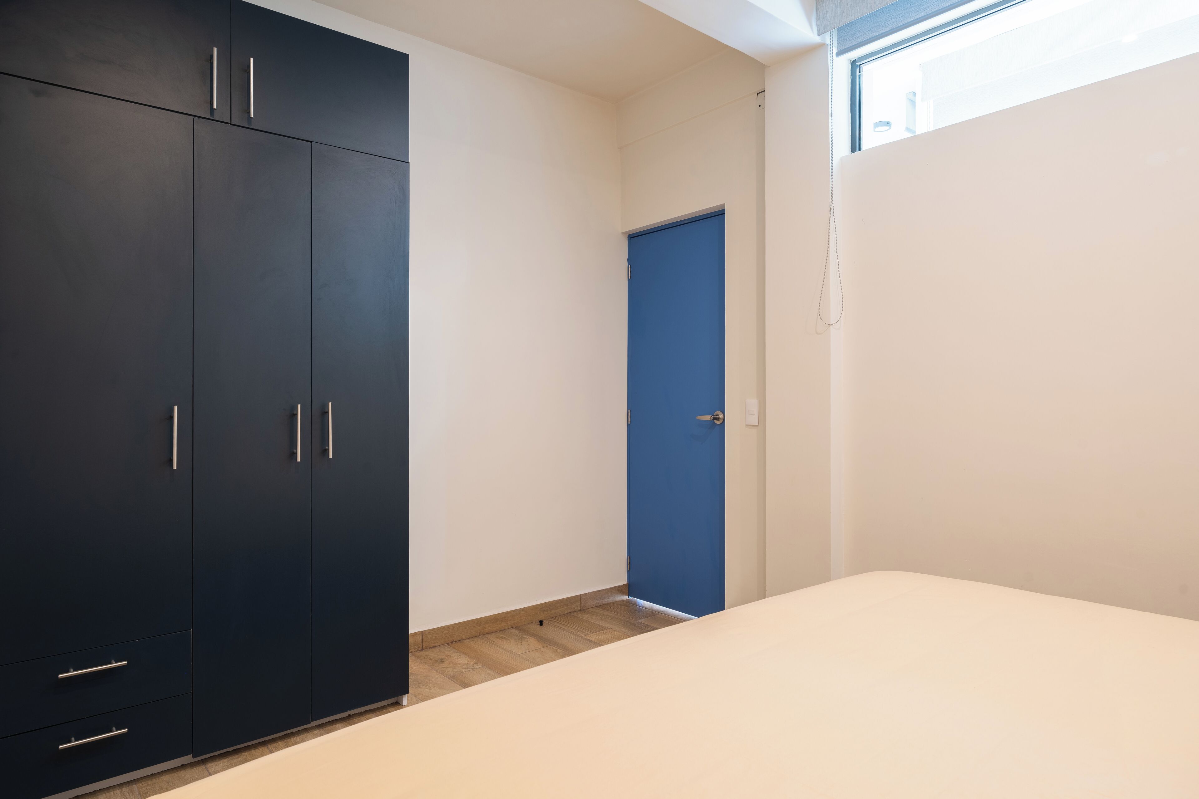 A bedroom with a large dark wardrobe, a blue door, and a bed.