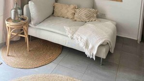 A modern living room with a beige sofa, a woven room divider, a round woven rug, and a glass vase with dried plants. - Palm Beach Vacaysuites - Garden Suite - Poolside (Noord)