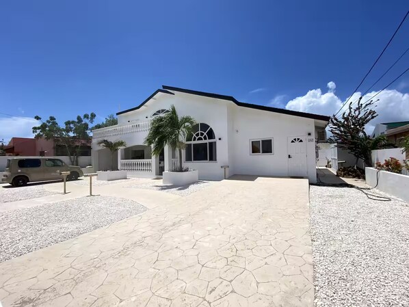 Una casa moderna de dos pisos con fachada blanca, un porche cubierto y un camino de entrada que lleva a la puerta principal.