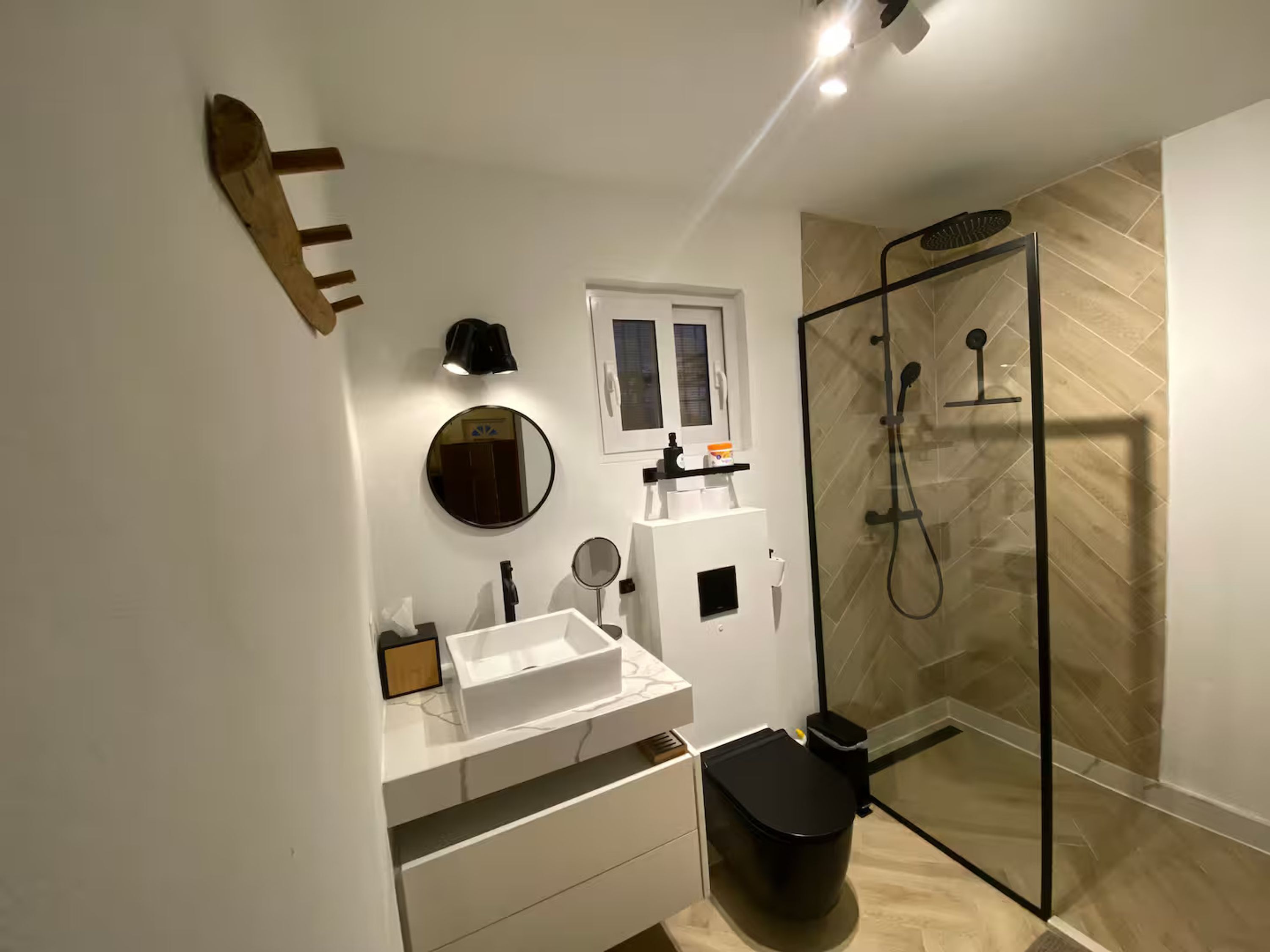A modern bathroom with a glass shower enclosure, a white sink, and a black toilet.