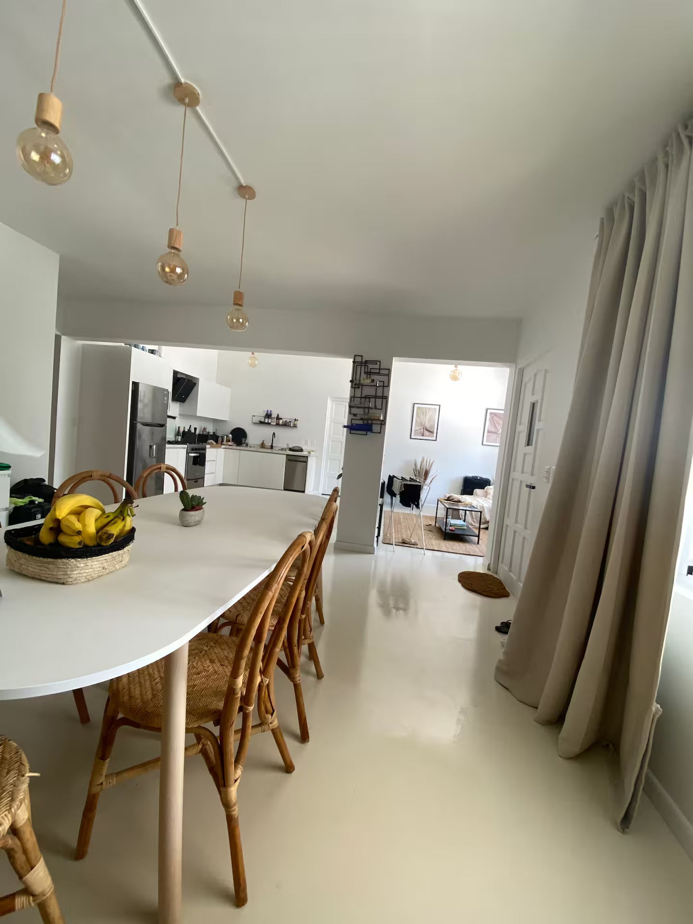 A modern kitchen with white cabinets, a stainless steel refrigerator, and a dining area with a white table and wicker chairs.