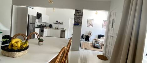 A modern kitchen with white cabinets, a stainless steel refrigerator, and a dining area with a white table and wicker chairs.