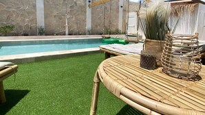 A pool area with artificial grass, a wicker lounge chair, and a stone wall. - Palm Beach Vacaysuites - Palm Suite 100m2 (Noord)