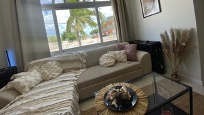 A living room with a large window, a sofa, a glass coffee table, and a framed picture on the wall. - Palm Beach Vacaysuites - Palm Suite 100m2 (Noord)