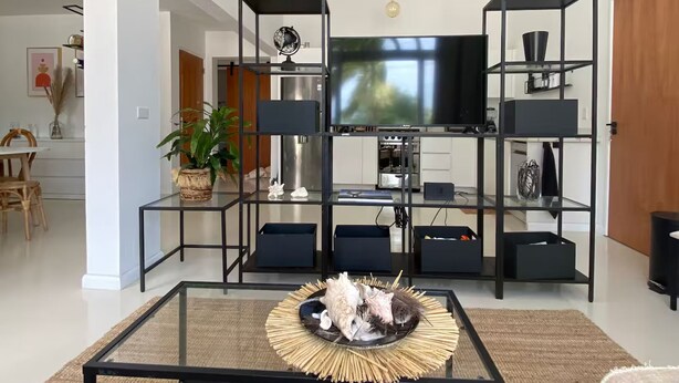 A modern living room with a black coffee table, a TV, and a black shelving unit with decorative items. - Palm Beach Vacaysuites - Palm Suite 100m2 (Noord)