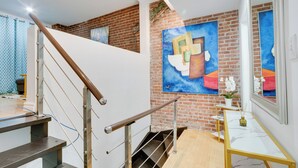 A modern interior with a staircase, a brick wall, and a painting of a figure holding books.