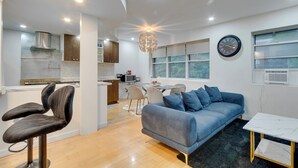 A modern kitchen with a dining area, a living room with a sofa and a coffee table, and a large window with a view.