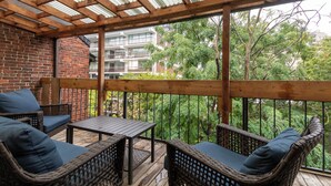 A covered patio with wicker furniture and a view of a brick building and trees.