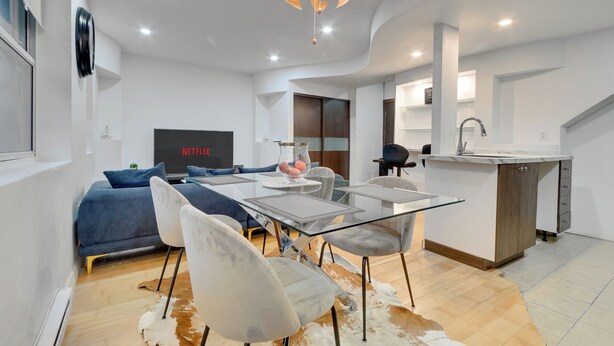 A modern living room with a glass dining table, sofas, and a TV displaying 'NETFLIX'.