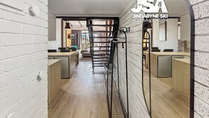Un couloir doté d’un plancher en bois, de murs en briques blanches et d’un escalier en métal. On y trouve deux comptoirs d’accueil, équipés d’ordinateurs et de chaises.