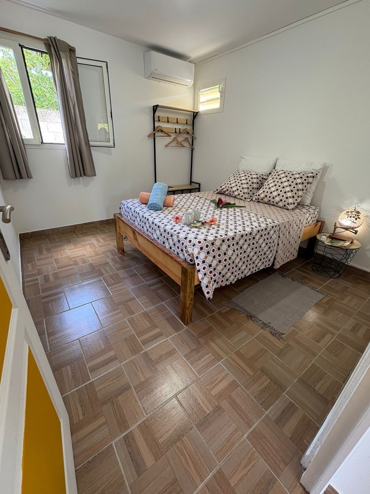 A bedroom with a bed, a bedside table, a hanging clothes rack, and a window with curtains.