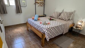 Een slaapkamer met een bed, nachtkastje, kledingrek en raam met gordijnen.