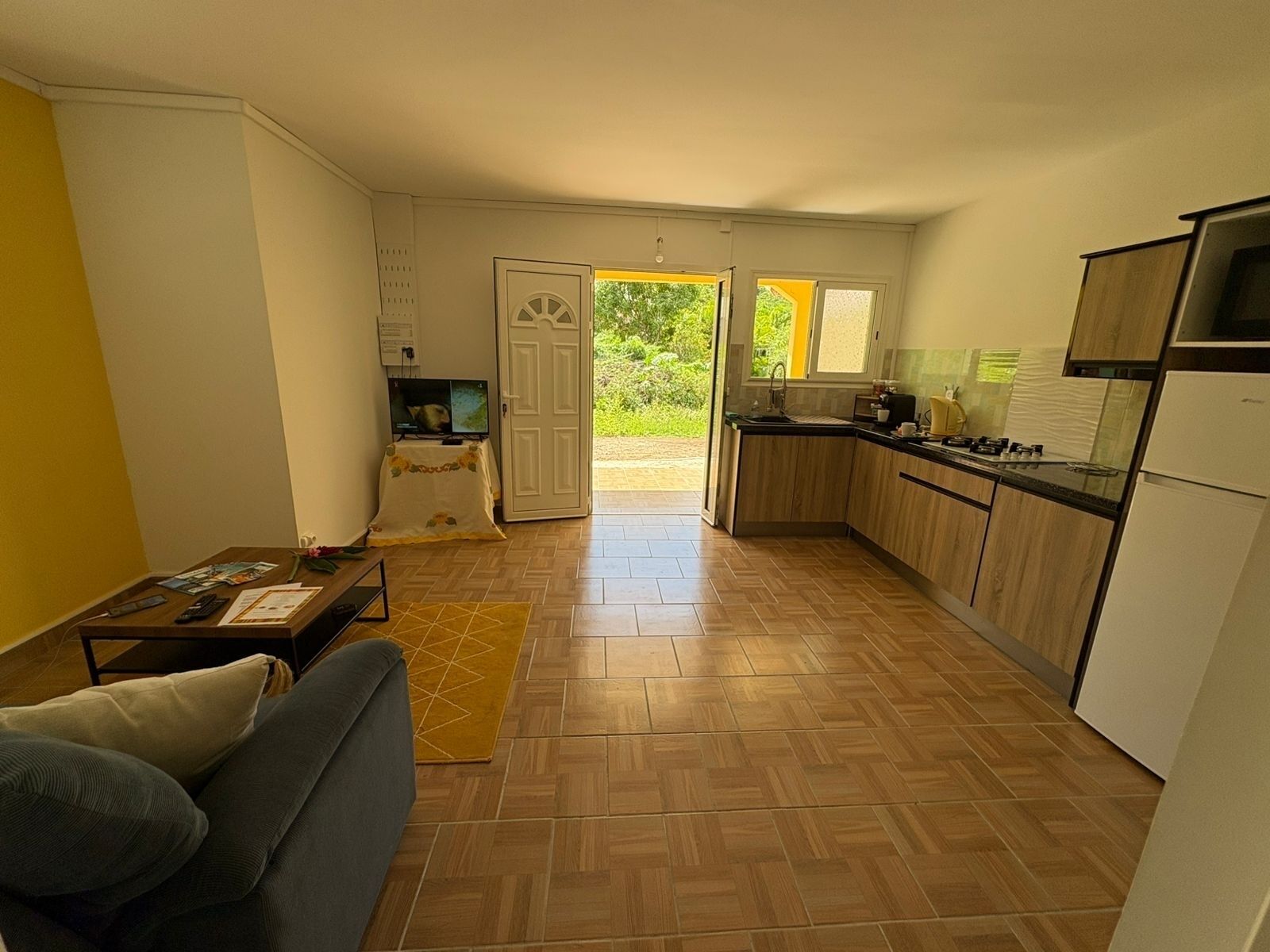 A compact living space with a sofa, a small table, a TV, and a kitchen area with a sink and stove.