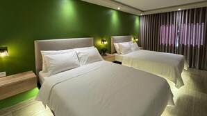 Une chambre d’hôtel avec deux lits, des murs verts et un rideau orné d’un motif violet et noir.