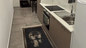 A compact kitchen with a built-in oven, a sink, and a stove. There is a dining area with a table and chairs, and a window with curtains. - City apartment no. 1 with comfort (Pforzheim)