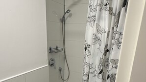 A small, tiled shower area with a showerhead, handheld shower, and a shower curtain with a leaf pattern. - City apartment no. 1 with comfort (Pforzheim)