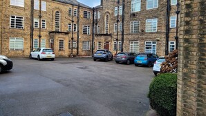 A parking area with several cars parked in front of a row of brick buildings with multiple windows and doors. - Sefton Park n Princes Park and Lark Lane the other end of Linnet and bus to LFC (Liverpool)