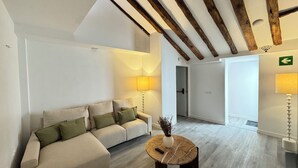 Un salon moderne avec un canapé, une table basse et une lampe. Une porte donne accès à une autre pièce, et un panneau indique la sortie.