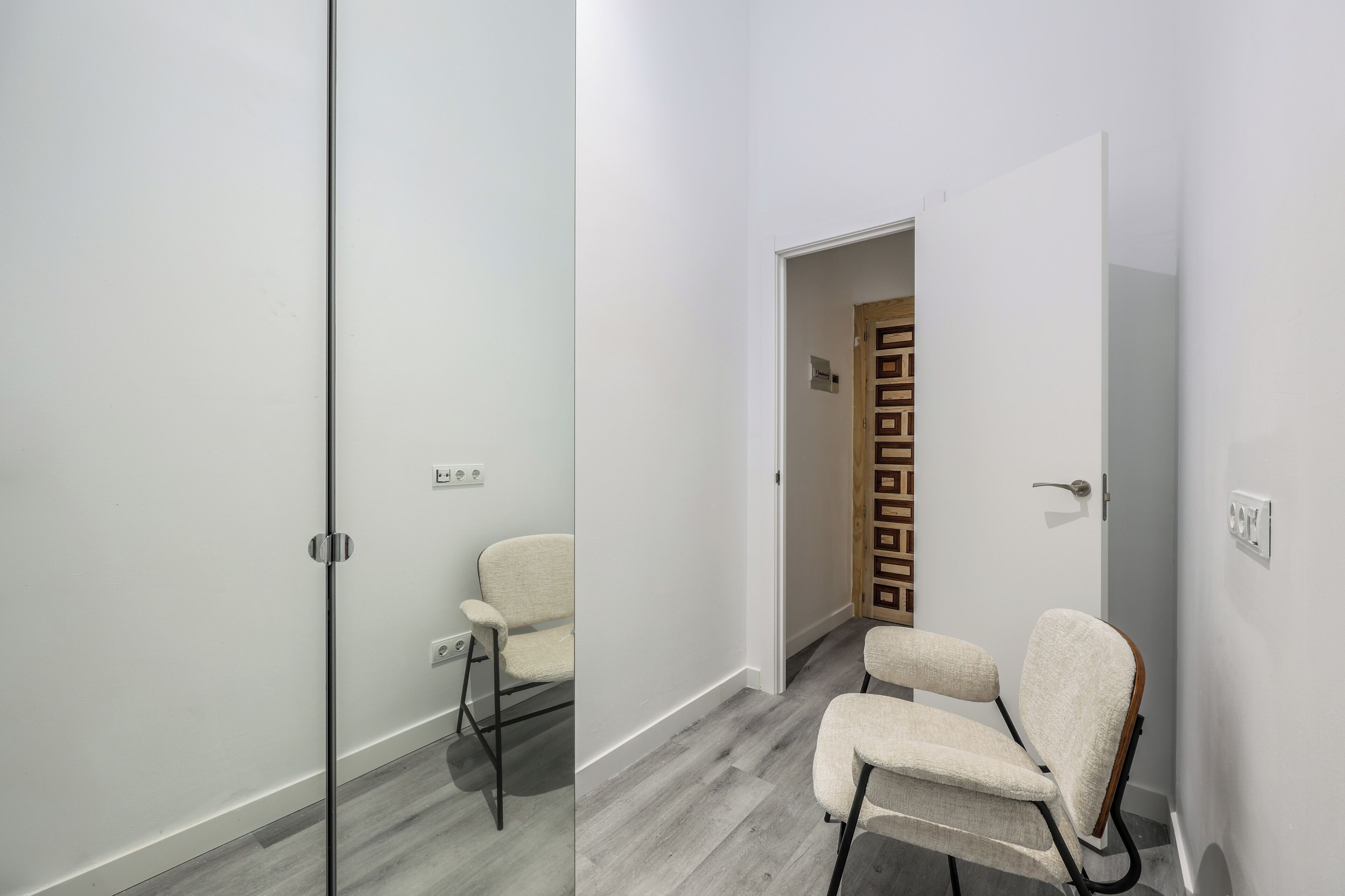 A modern, minimalist room with a glass partition, a wooden door, and a single beige chair.