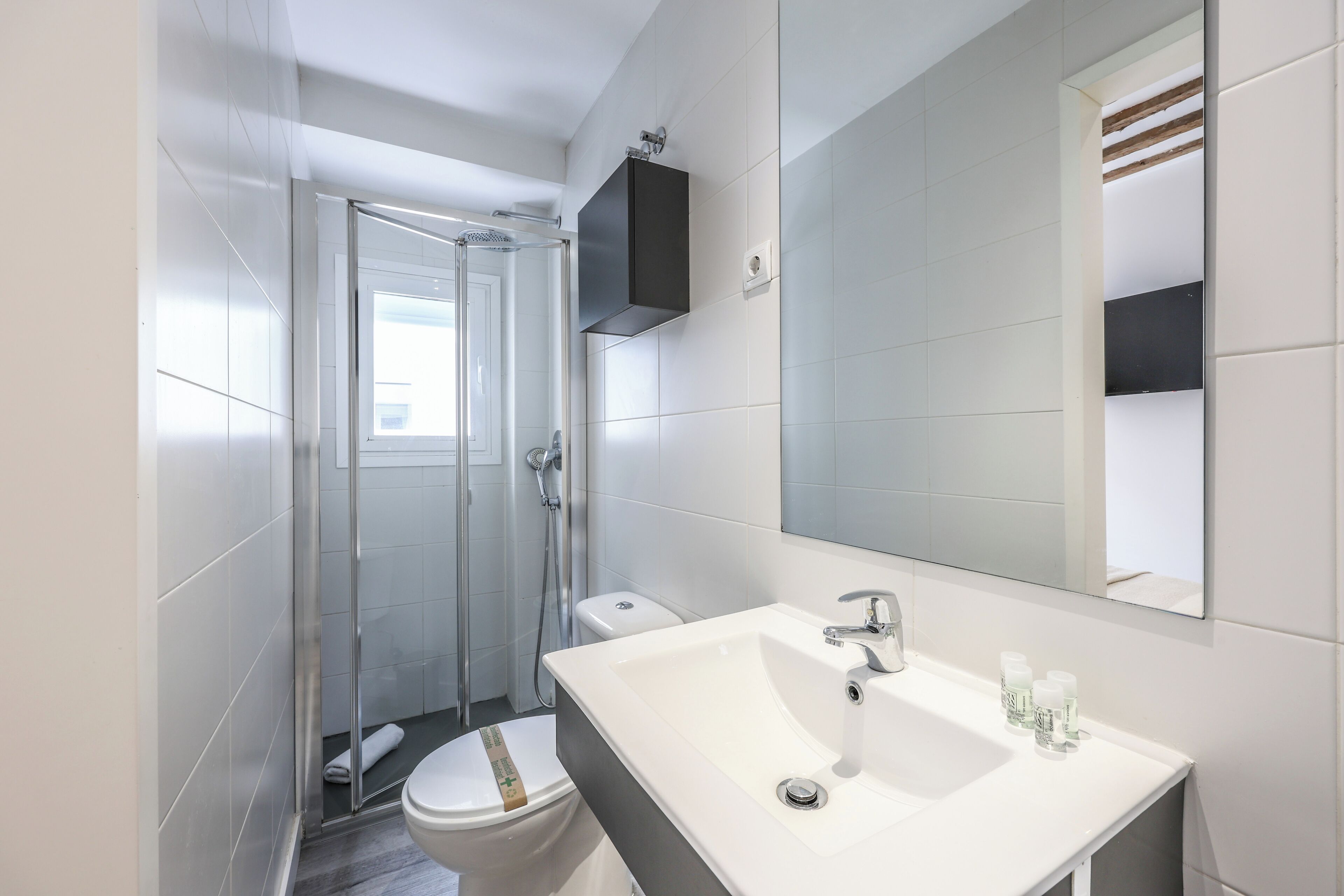 Un baño moderno con cabina de ducha de vidrio, un lavabo blanco y un espejo grande.