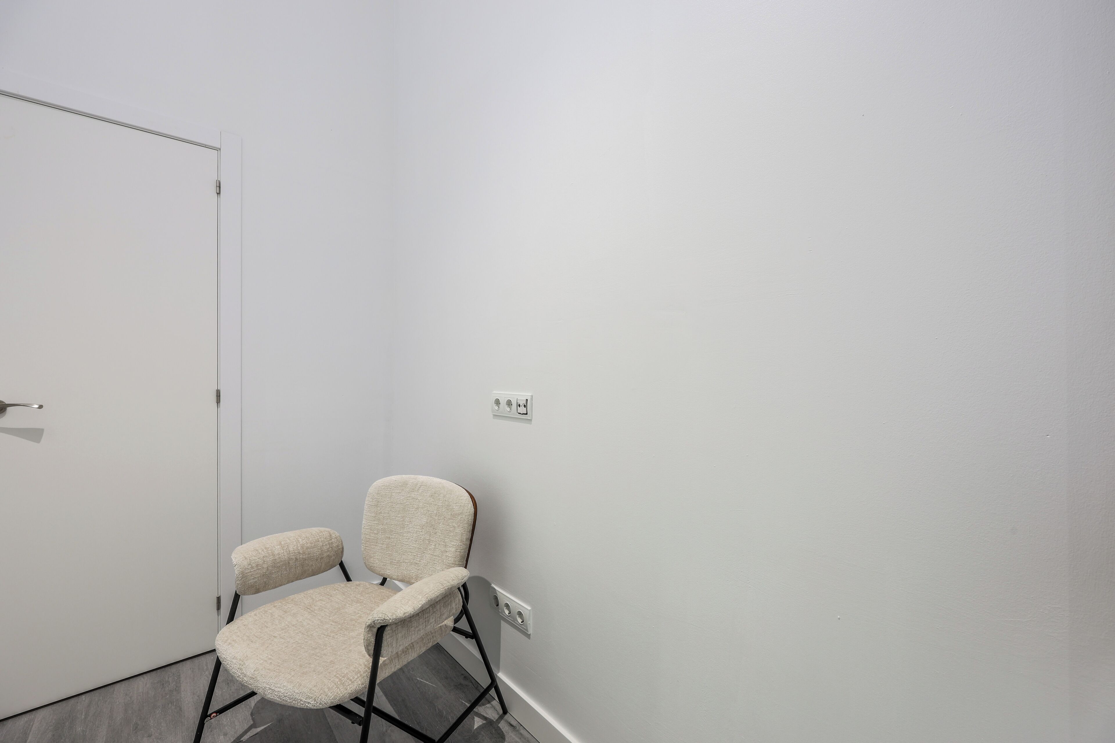 A small, empty room with a white door, a white wall, and a single chair.