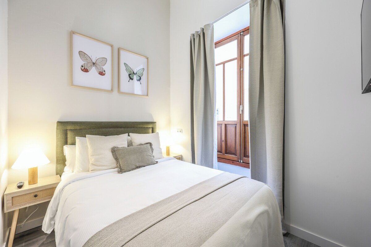 A neatly made bed with a headboard, two bedside lamps, and two framed butterfly pictures on the wall.