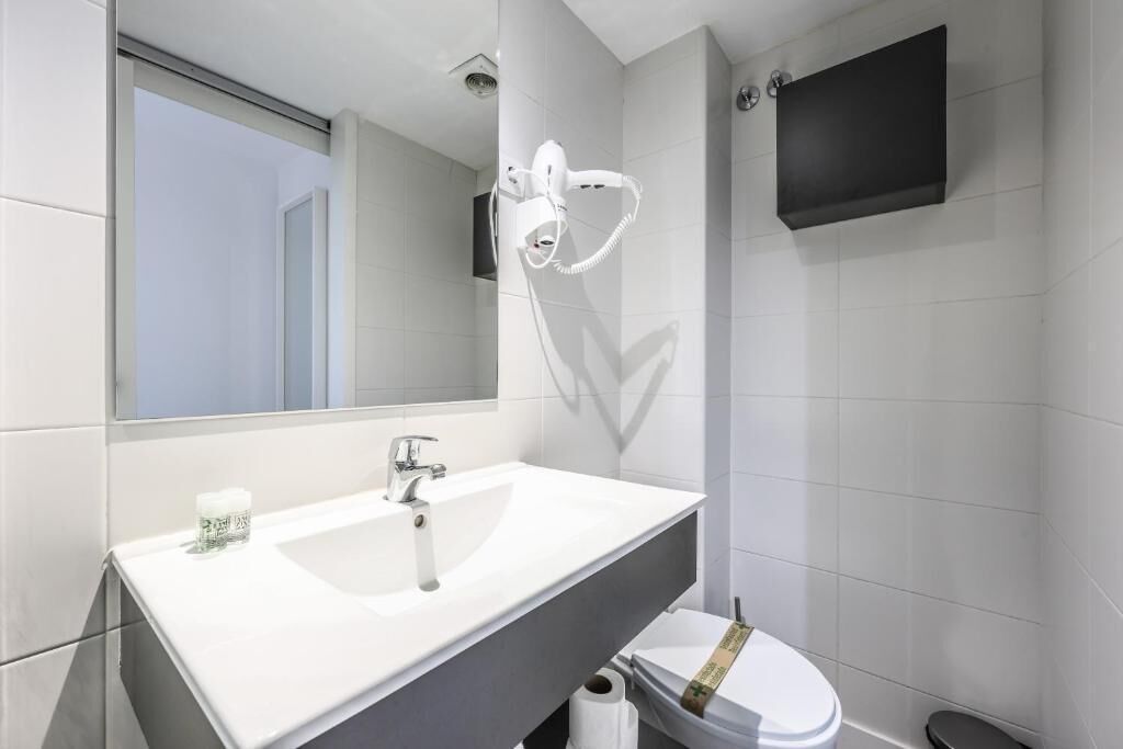 A modern bathroom with a white sink, a mirror, a hairdryer, and a toilet.
