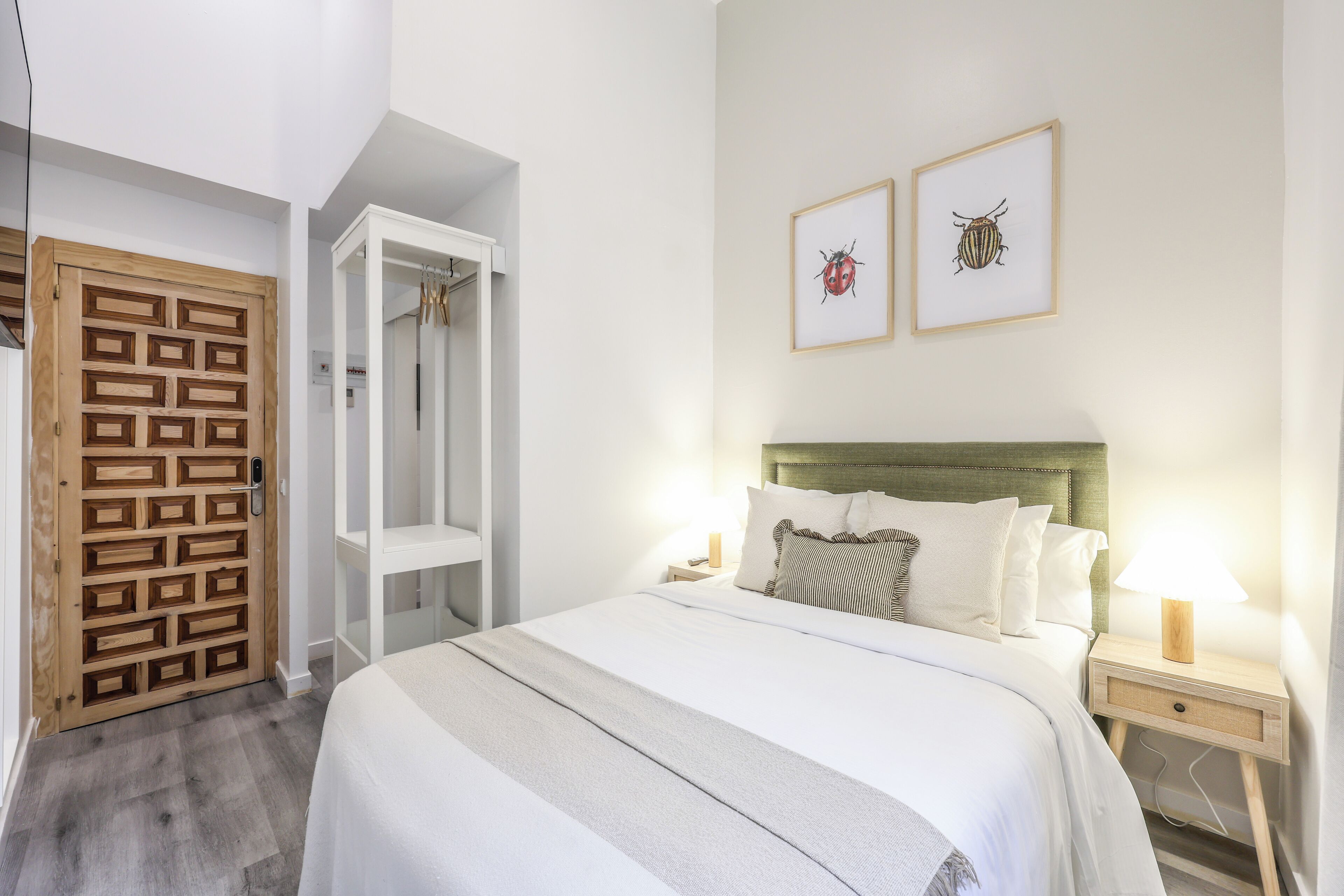 Un dormitorio con una cama, mesitas de noche, un armario de madera y dos cuadros en la pared.