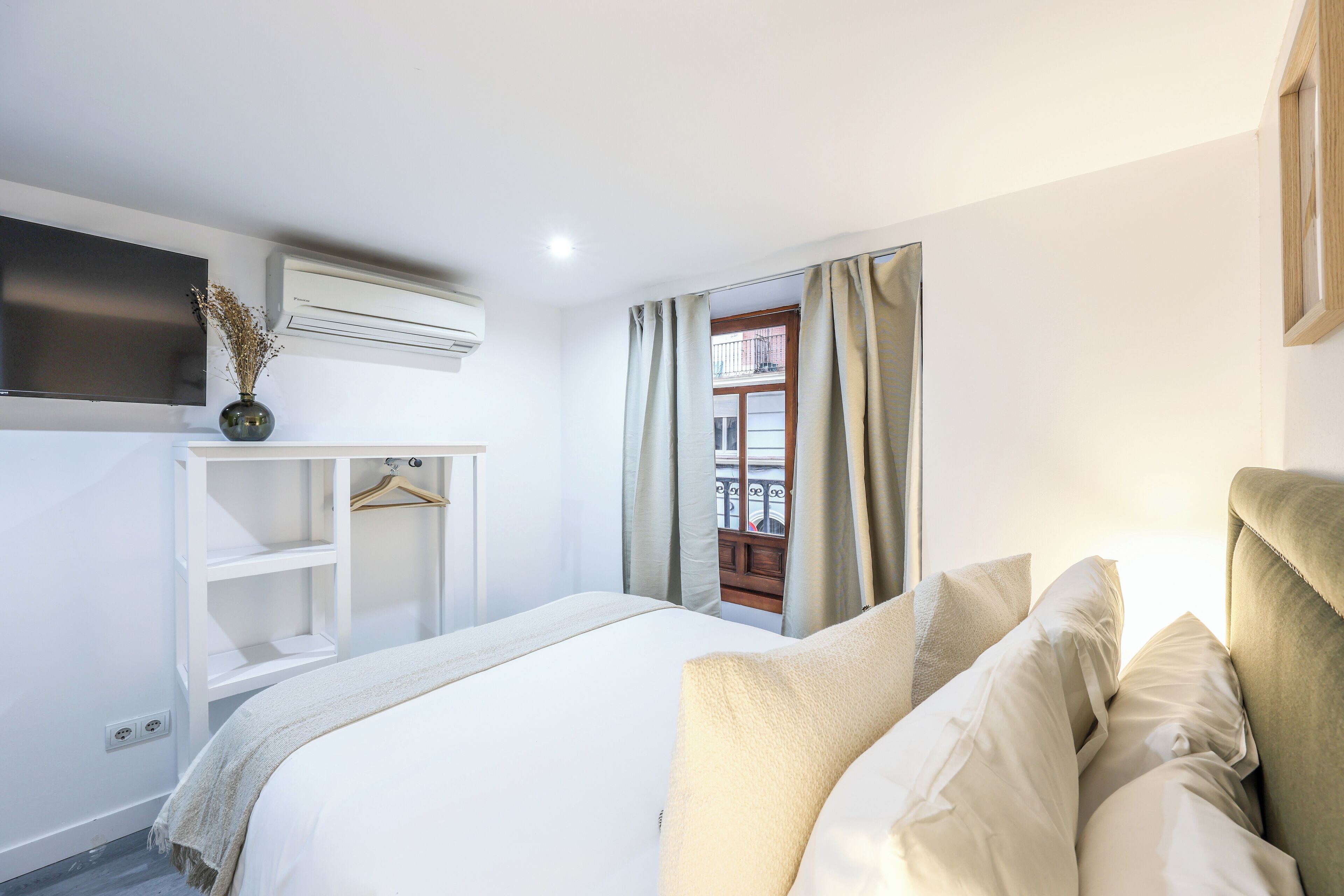 A bedroom with a bed, a TV, a wardrobe, and a window with curtains.
