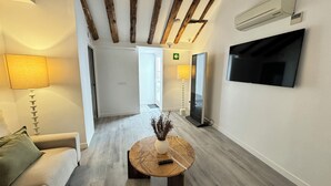 Un couloir d’hôtel avec un canapé, une table ronde ornée d’un vase, un téléviseur fixé au mur et un plafond en bois.