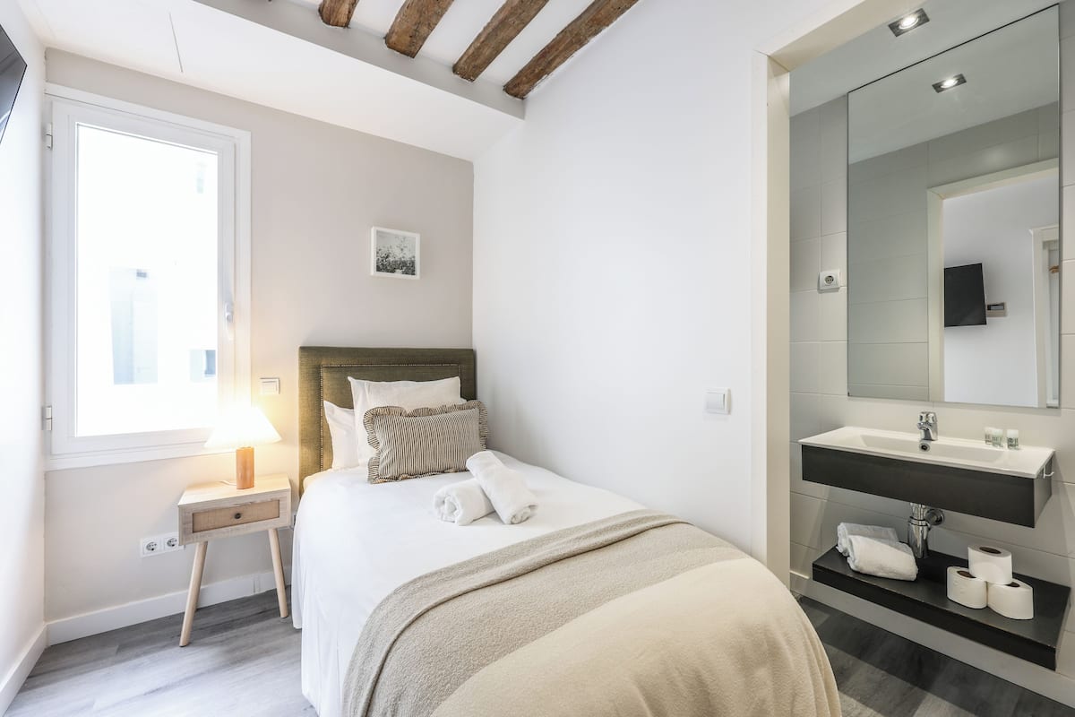 Une chambre à coucher comprenant un lit, une table de chevet et une lampe, ainsi qu’une salle de bain avec un lavabo et un miroir.