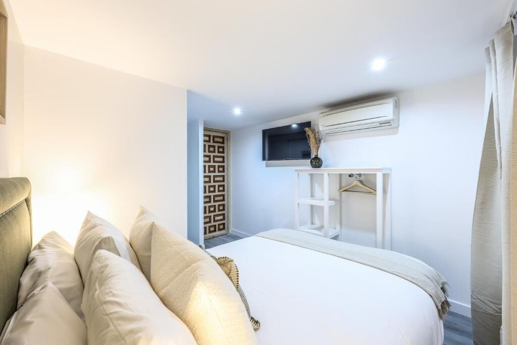 A hotel room with a bed, a TV mounted on the wall, an air conditioning unit, and a door with a geometric pattern.