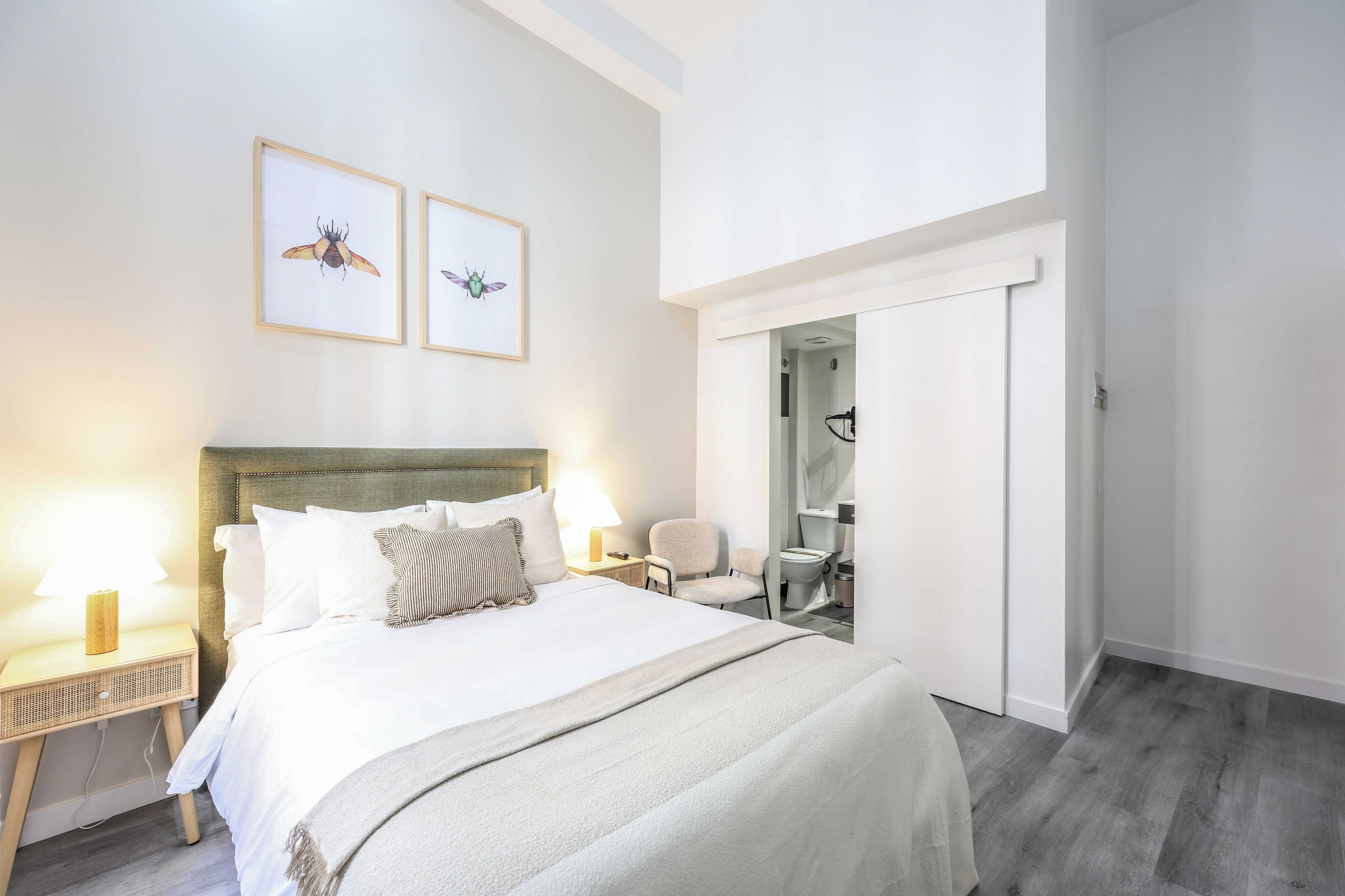A neatly arranged hotel room with a large bed, bedside lamps, a chair, and a door leading to a bathroom.