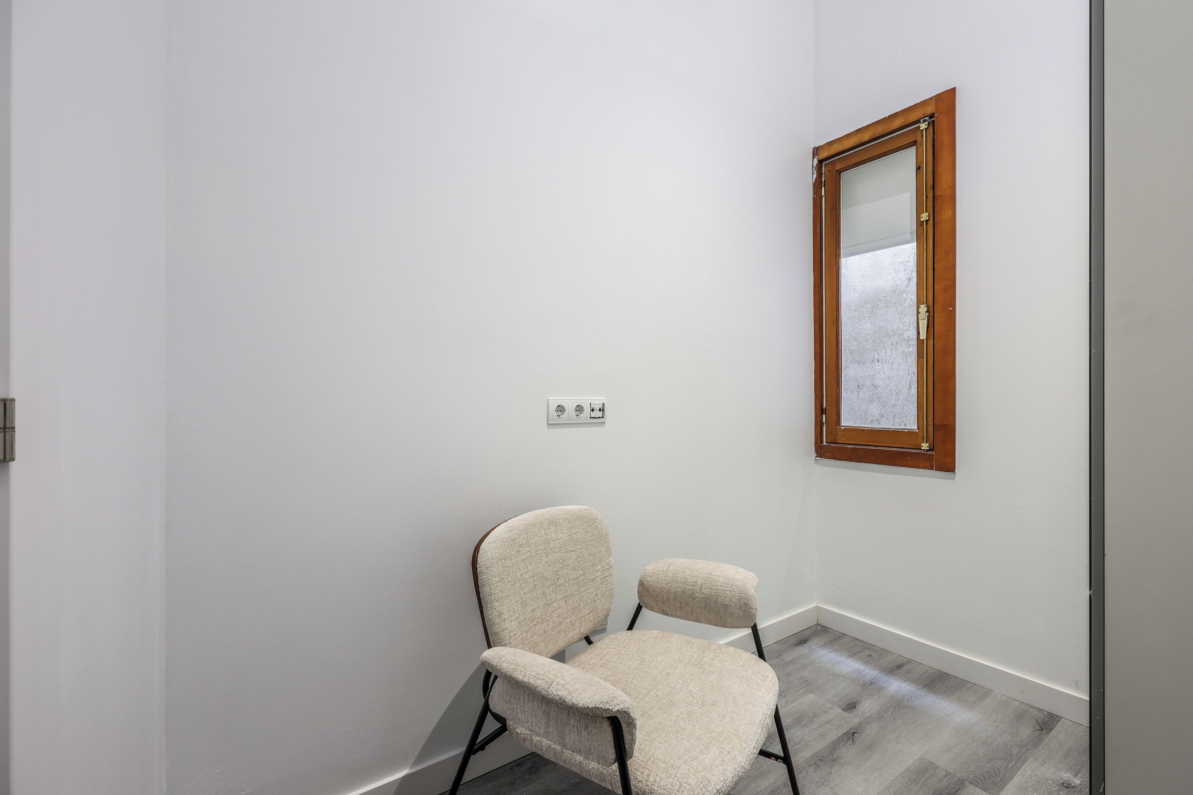 A room with a white wall, a wooden-framed mirror, and a beige chair.