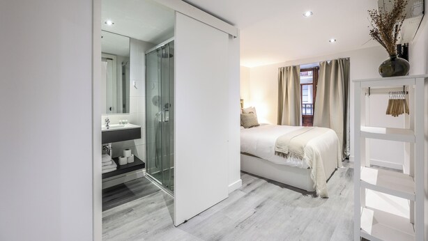 Une chambre moderne avec une douche en verre, un lit blanc et une table de chevet.