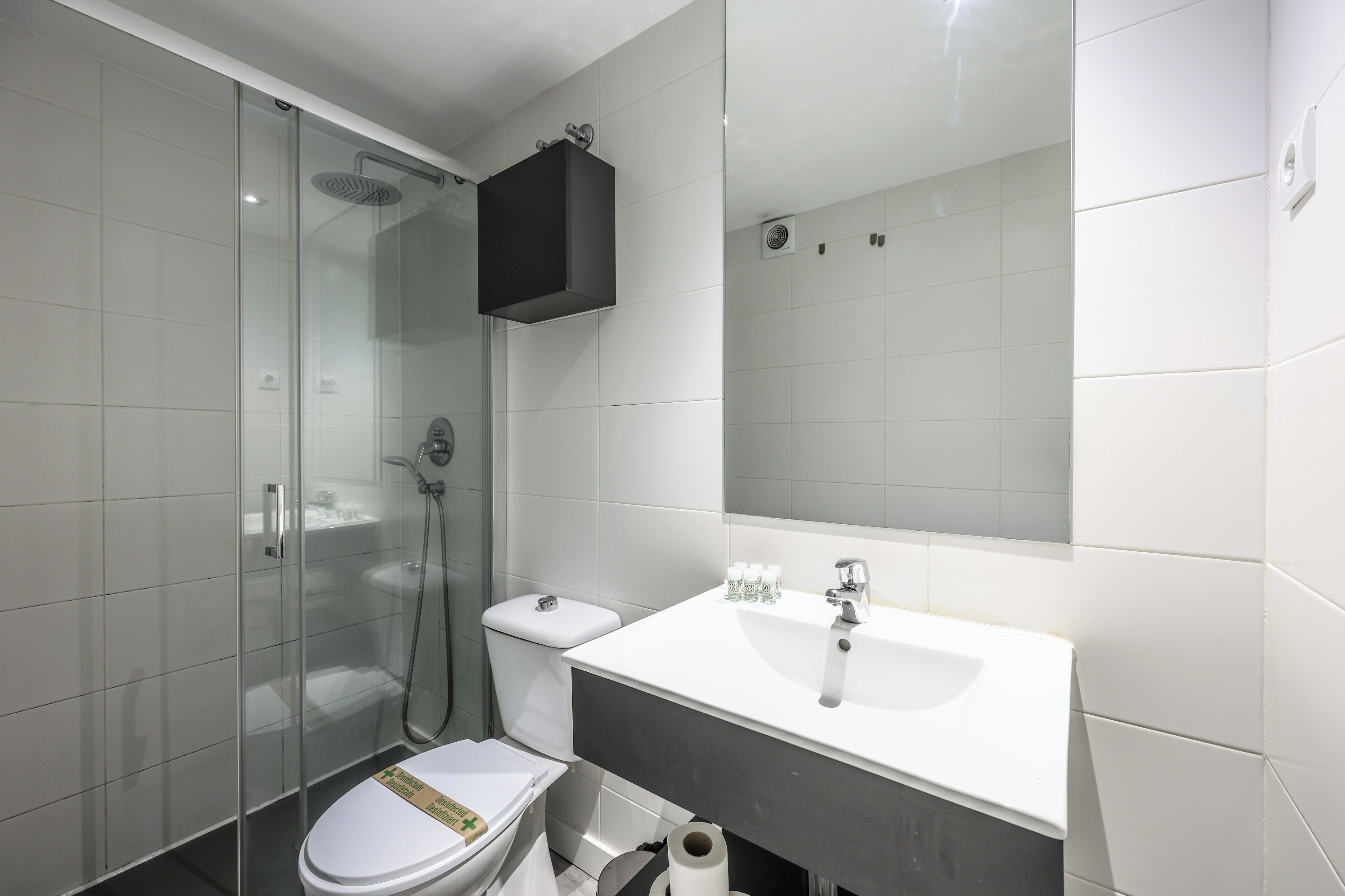 A modern bathroom with a glass shower enclosure, a white toilet, a white sink, and a dark-colored cabinet.