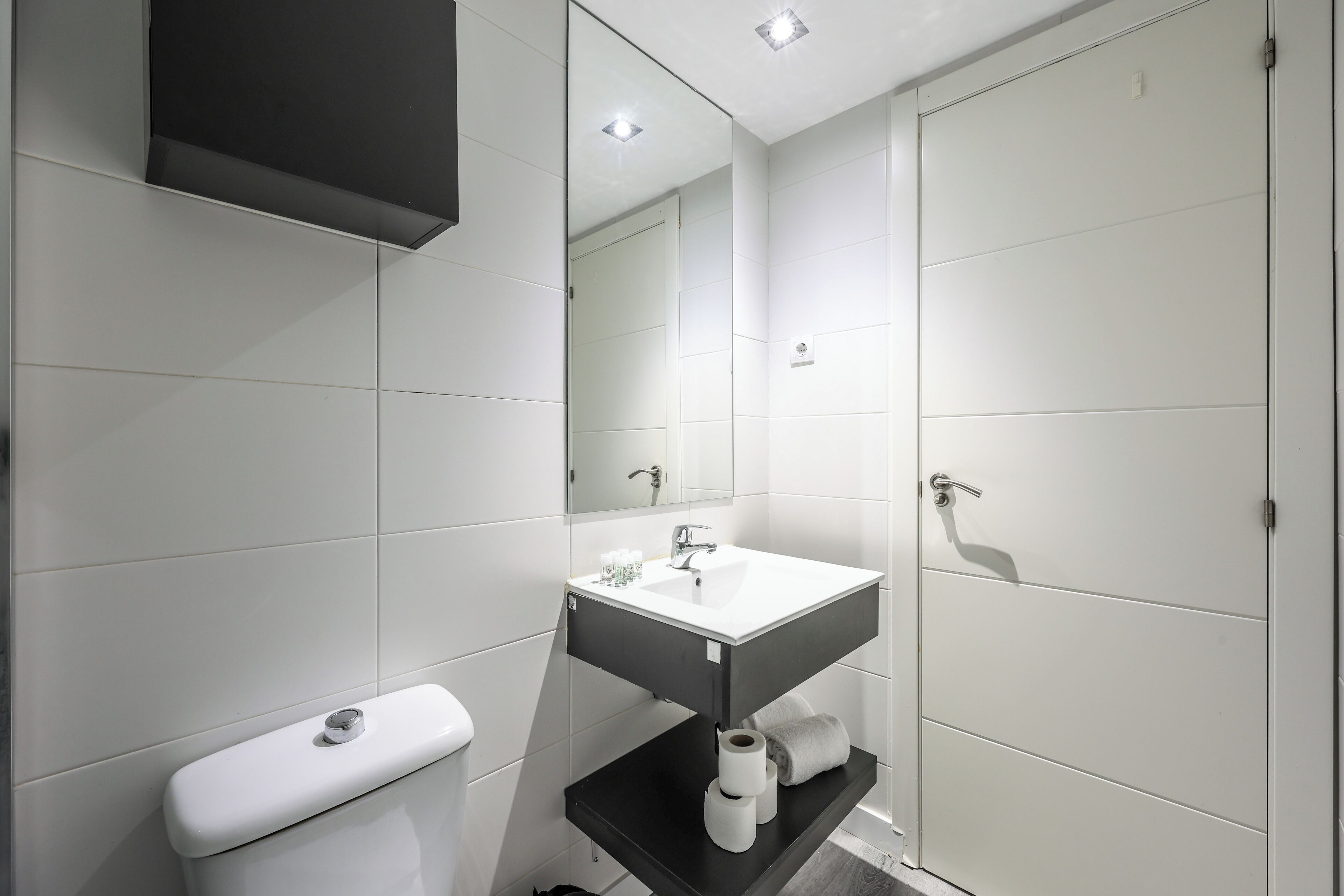 Un baño moderno con un inodoro blanco, un lavamanos negro y un espejo encima.