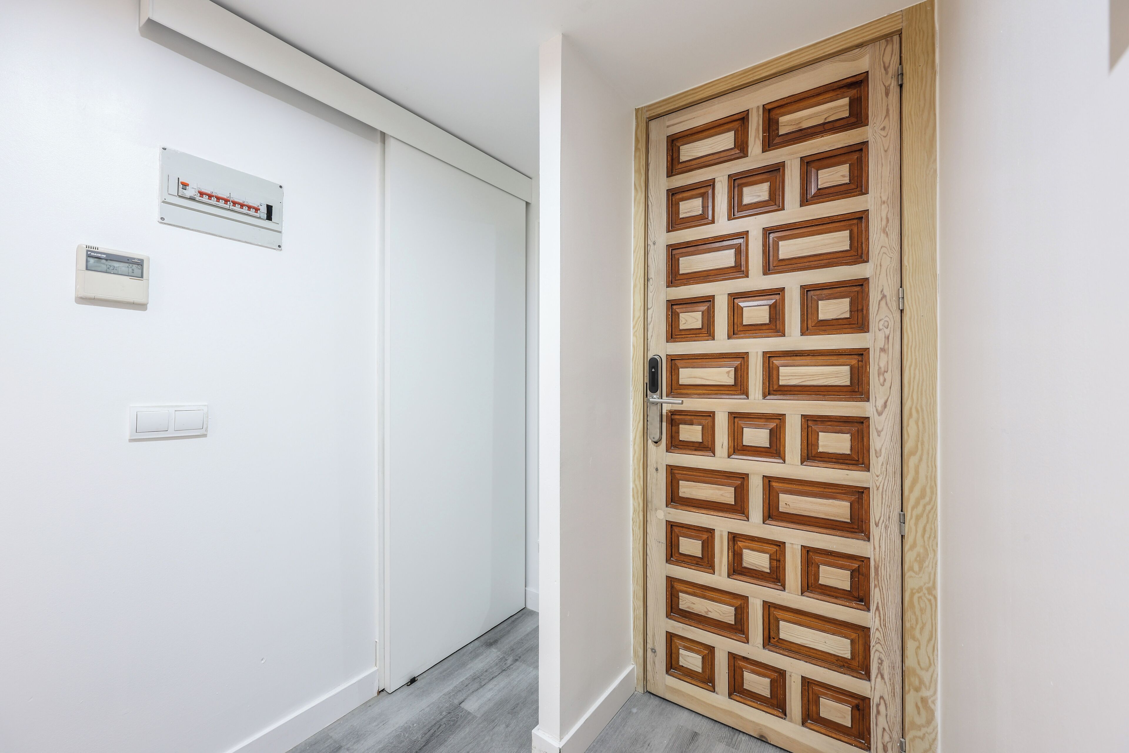 Un couloir avec une porte en bois, un interrupteur et un thermostat fixés au mur.