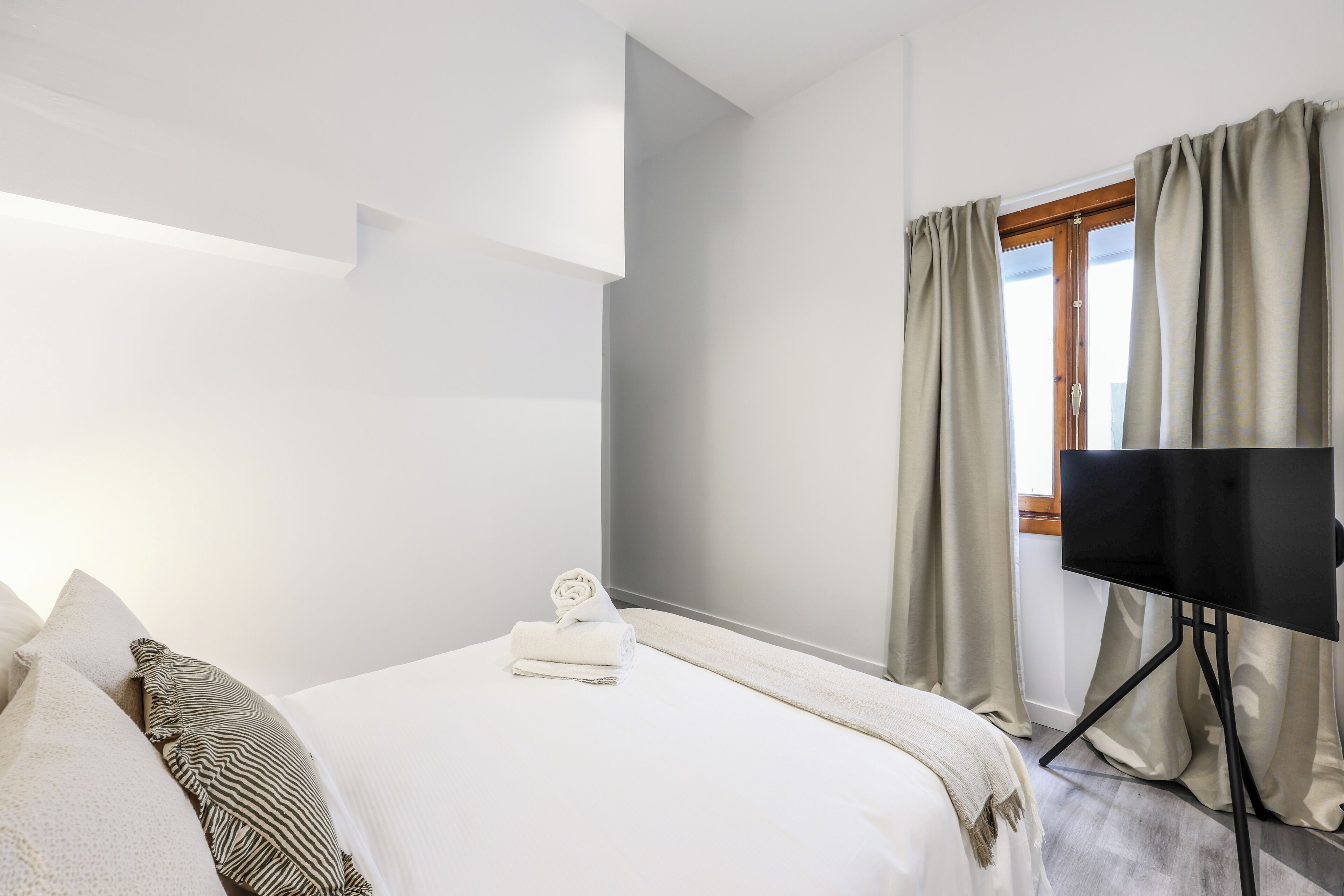 Une chambre d’hôtel avec un lit, des oreillers, un téléviseur posé sur un meuble et une fenêtre avec des rideaux.